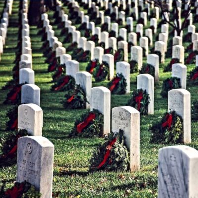 Rows of military headstones decorated with holiday wreaths in a cemetery