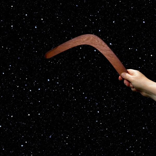 Hand holding a wooden boomerang against a star-filled space background
