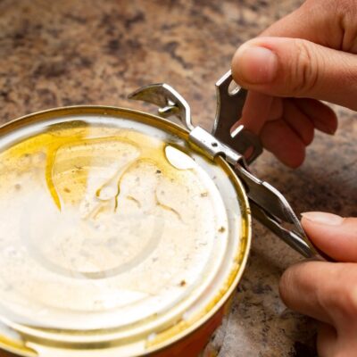 Person using a manual can opener on a sealed metal can