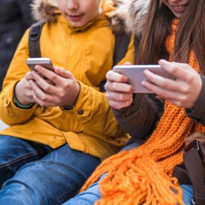 Two children in winter clothing using smartphones side by side