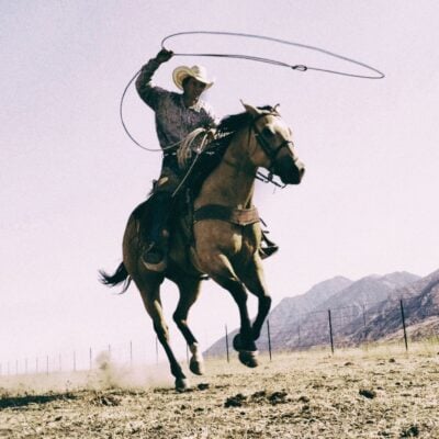Cowboy Euclides Guterrez on horseback swinging a lasso in an open field