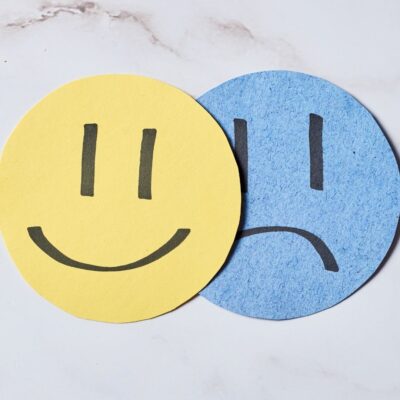 Yellow happy face overlapping a blue sad face on paper cutouts