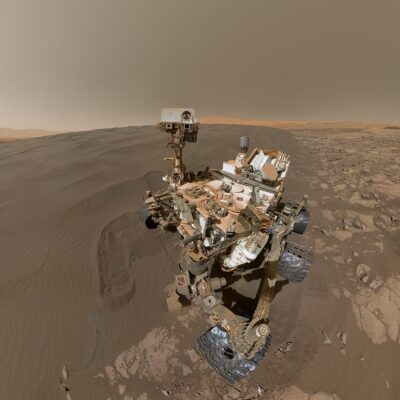 Mars Curiosity rover on rocky, sandy surface with wheel tracks visible