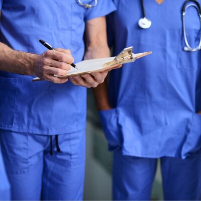 Two doctors in blue scrubs reviewing a clipboard