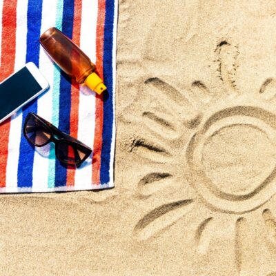 Sunglasses, sunscreen, and phone on striped towel beside sun drawing in sand