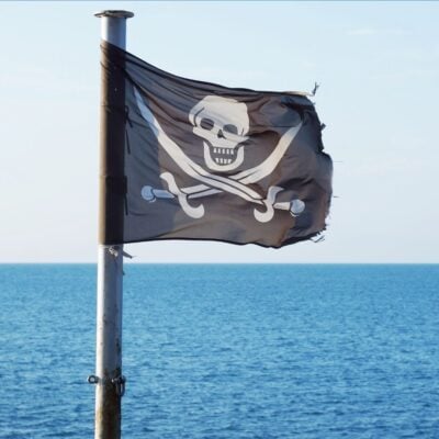 Black pirate flag with skull and crossed swords flying over the sea