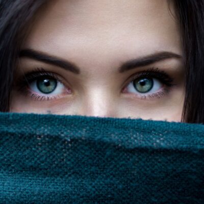 Close-up of a woman’s blue-green eyes partially covered by a dark green scarf
