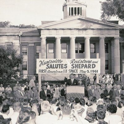 Crowd gathered in front of building with banner honoring Alan Shepard’s spaceflight