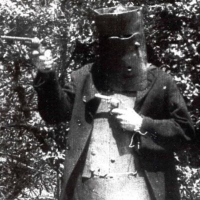 Character in metal armor pointing a pistol in a forest scene from The Story of the Kelly Gang