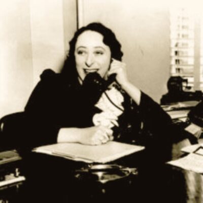 Woman speaking into a vintage microphone at a desk with papers