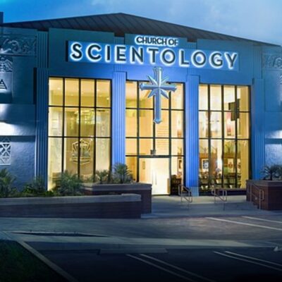 Exterior of a Church of Scientology building with illuminated signage and cross symbol