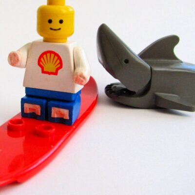 LEGO surfer figure on red surfboard next to toy shark with open mouth