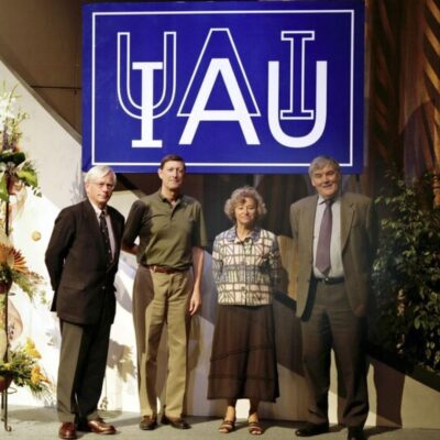 Four people standing under a large International Astronomical Union sign