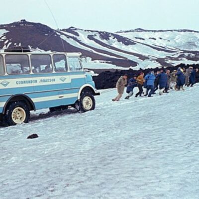 Group of people pulling a stuck bus in snowy Icelandic terrain