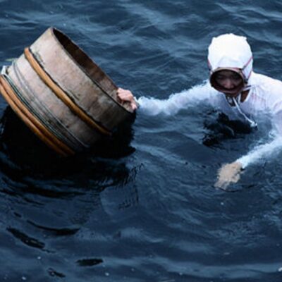 Ama diver in traditional white outfit holding wooden barrel in the sea