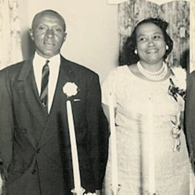 Elderly couple dressed formally, standing together holding candles and smiling
