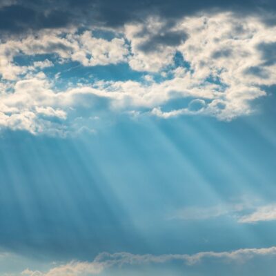 Sunlight beams shining through scattered clouds in a blue sky