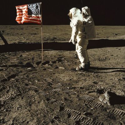 Apollo astronaut stands near American flag on the Moon with visible footprints on lunar surface