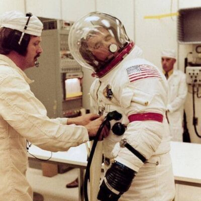Apollo astronaut suited up while technician adjusts equipment on spacesuit