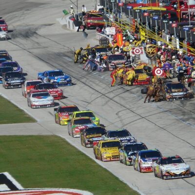 NASCAR pit crews in action as cars line up during a race pit stop
