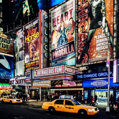 Broadway theater billboards including War Horse, Priscilla, and Chicago above yellow taxis
