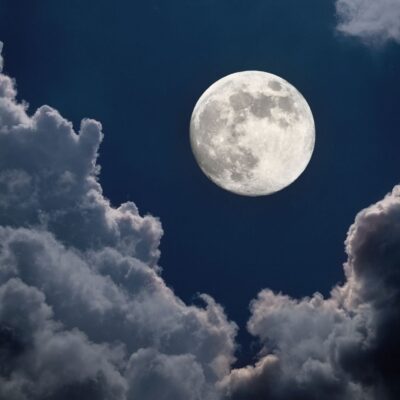 Full moon shining brightly between scattered dark clouds