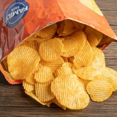 Open family-size bag of ridged potato chips spilling onto wooden surface
