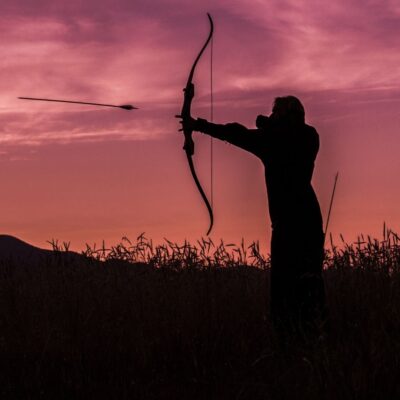 Archer releasing an arrow at sunset in a field