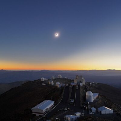 Total solar eclipse above observatories on a mountain at sunset