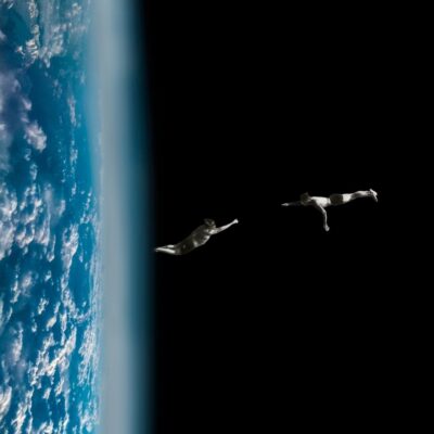 Two human figures floating in space near Earth's atmosphere