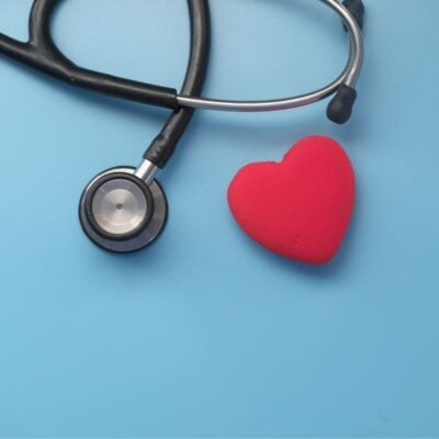 Stethoscope next to a red heart-shaped object on blue background