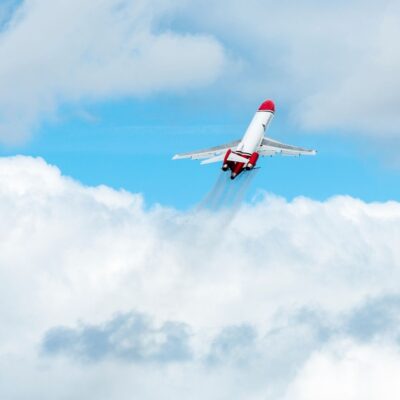 A Boeing 727 with red accents ascending above white clouds