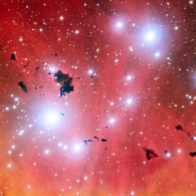 Bright stars and dark interstellar clouds in a glowing red nebula
