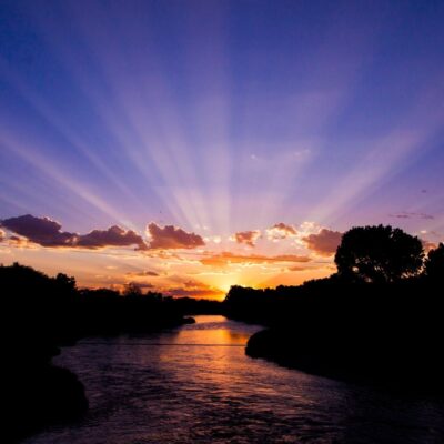 Sunset over a river with scattered clouds and silhouetted trees