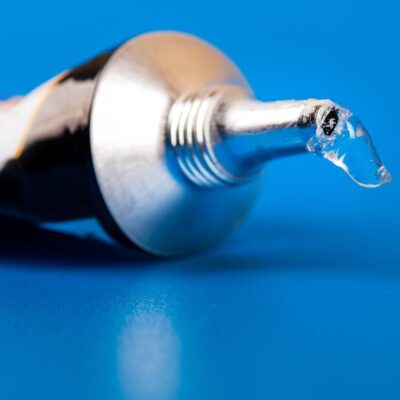 Close-up of superglue oozing from a metal tube on blue surface