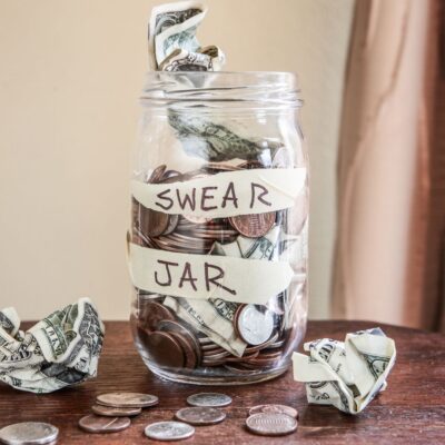 Glass jar labeled 'Swear Jar' filled with coins and crumpled dollar bills
