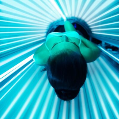 Woman lying inside a lit tanning bed wearing a white top