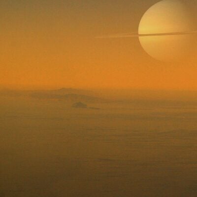 View of Saturn in the sky above Titan’s orange, misty landscape with distant hills