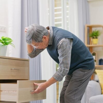 Older man looking confused while searching a drawer in a brightly lit room