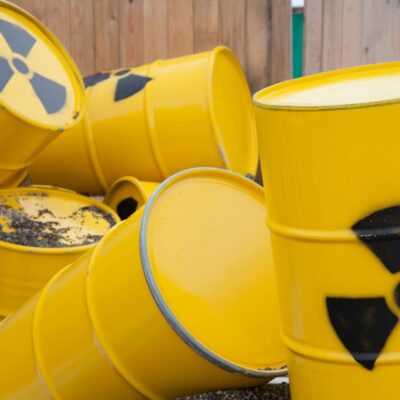 Yellow barrels with radioactive warning symbols piled against a wooden fence