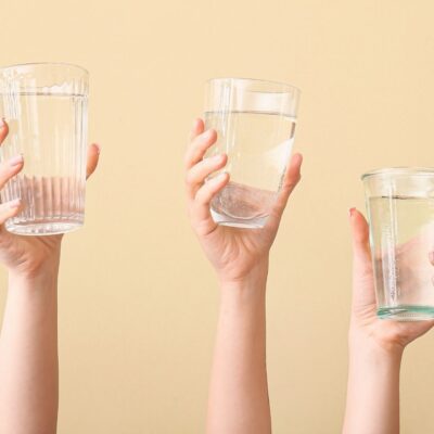 Three hands holding up clear glasses of water against a beige background