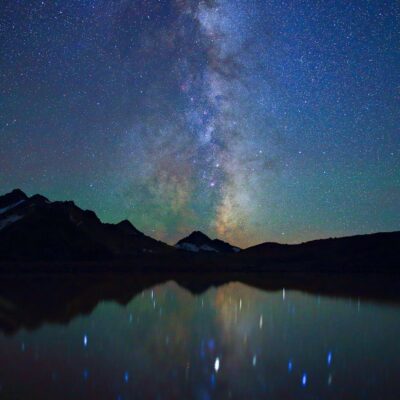 Star-filled night sky with Milky Way over mountains reflected in calm water