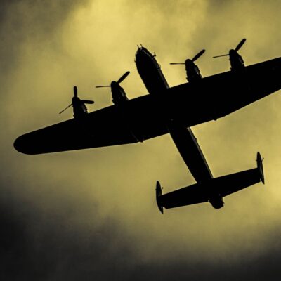 Silhouette of a four-engine military bomber flying against a cloudy sky