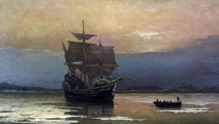 A ship with tall sails on calm waters during sunset, with a small boat carrying people nearby, related to the Pilgrims