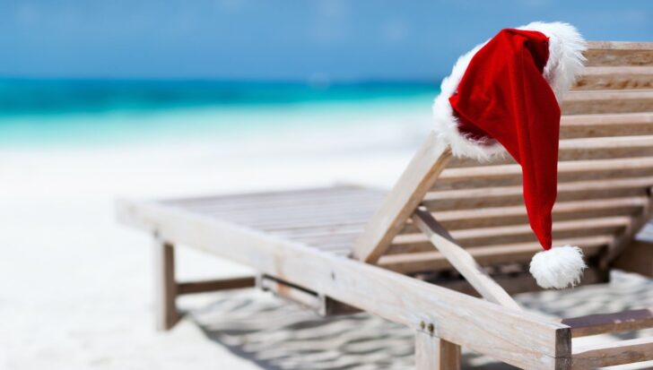 Santa hat draped over a wooden beach lounge chair with the ocean in the background