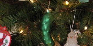 Christmas tree with a green pickle ornament and a snowman decoration among branches and lights