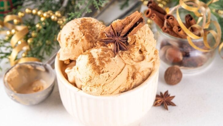 Creamy ice cream scoops in a bowl sprinkled with spices, accompanied by cinnamon sticks, star anise, and a festive evergreen background, highlighting cold desserts for Christmas in Australia