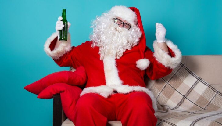Santa Claus in a relaxed pose on a sofa holding a green bottle