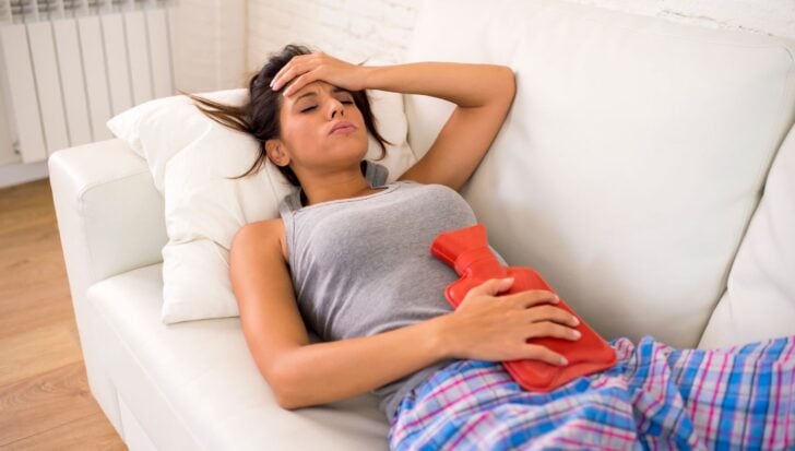 Woman lying on a couch holding a red hot water bottle on her abdomen