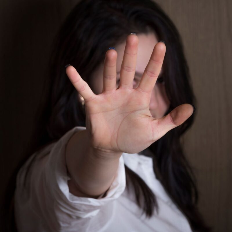 Woman with long dark hair holding hand up to block the camera